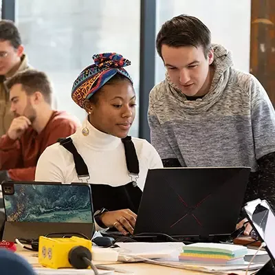 Students collaborating at a table viewing a laptop.